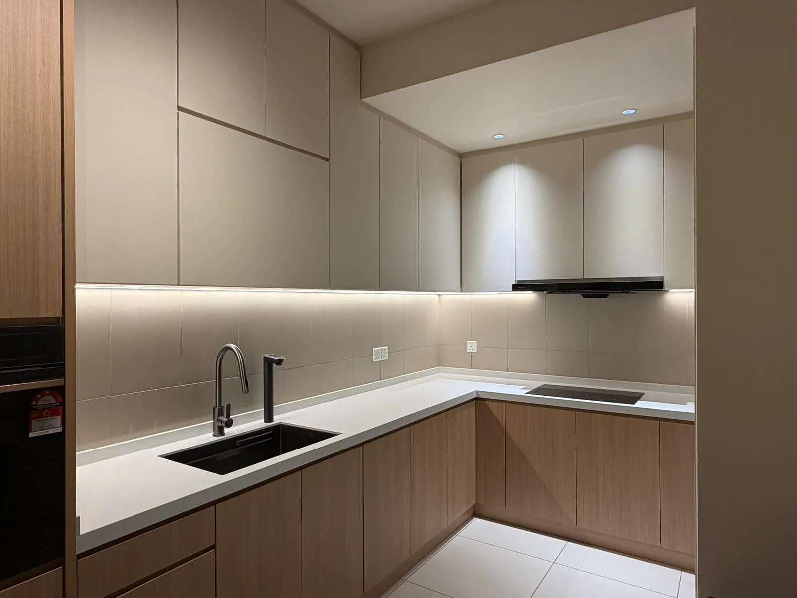 L-shaped condo kitchen with oak-look base cabinets, plain light upper doors and LED strip under the wall units, Kaia Heights