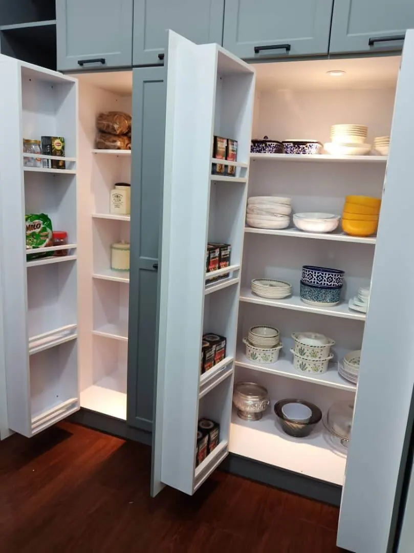 Unit pantry tarik keluar dibuka dalam dapur kelabu, menunjukkan rak sempit berisi balang dan rak tinggi berisi pinggan