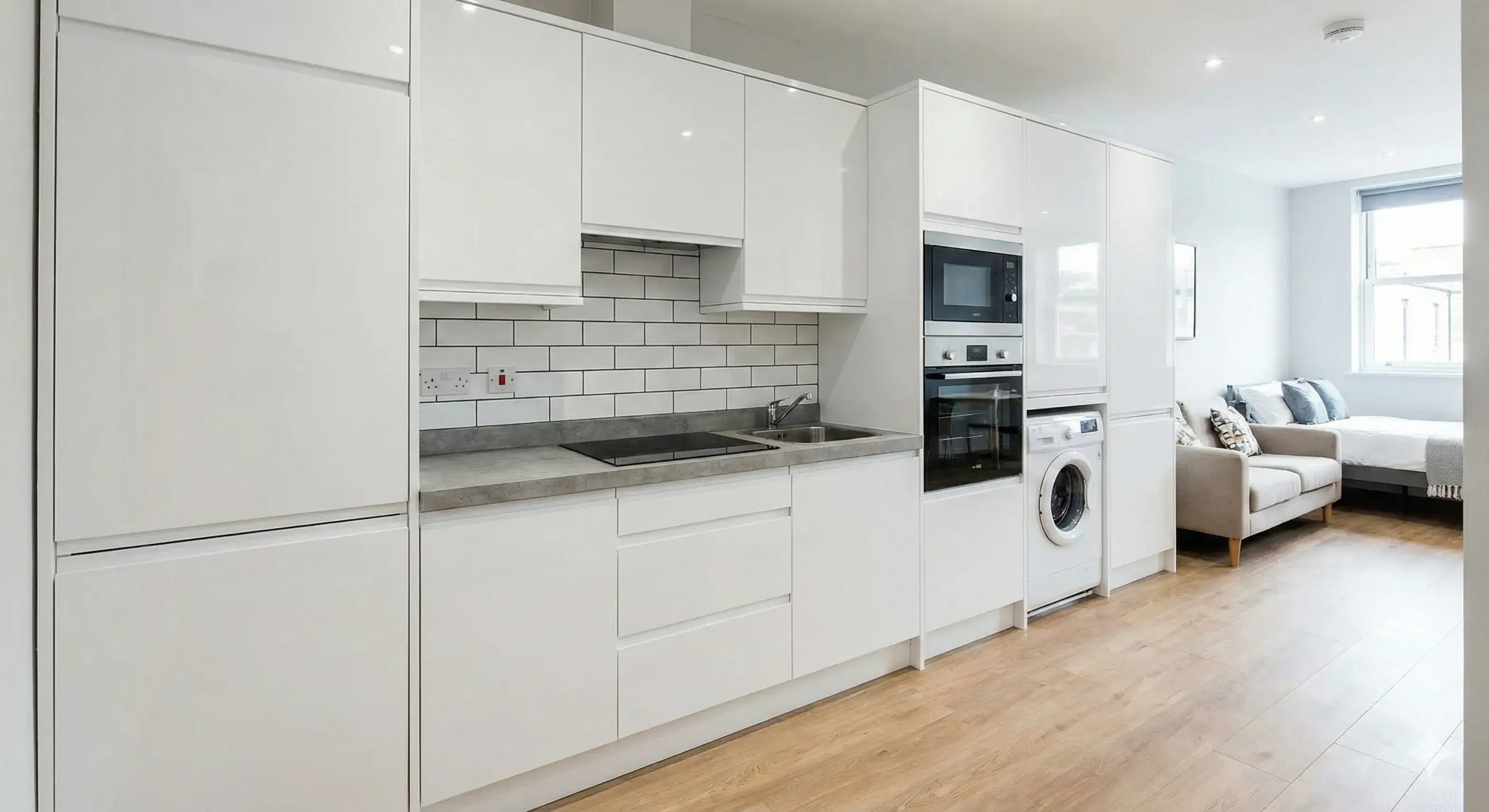 Compact straight kitchen layout in a studio apartment with integrated appliances.