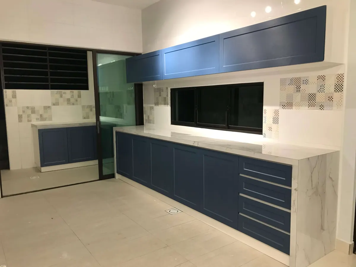 Straight kitchen run with navy shaker-style cabinets, white marble-look worktop and a window above the counter