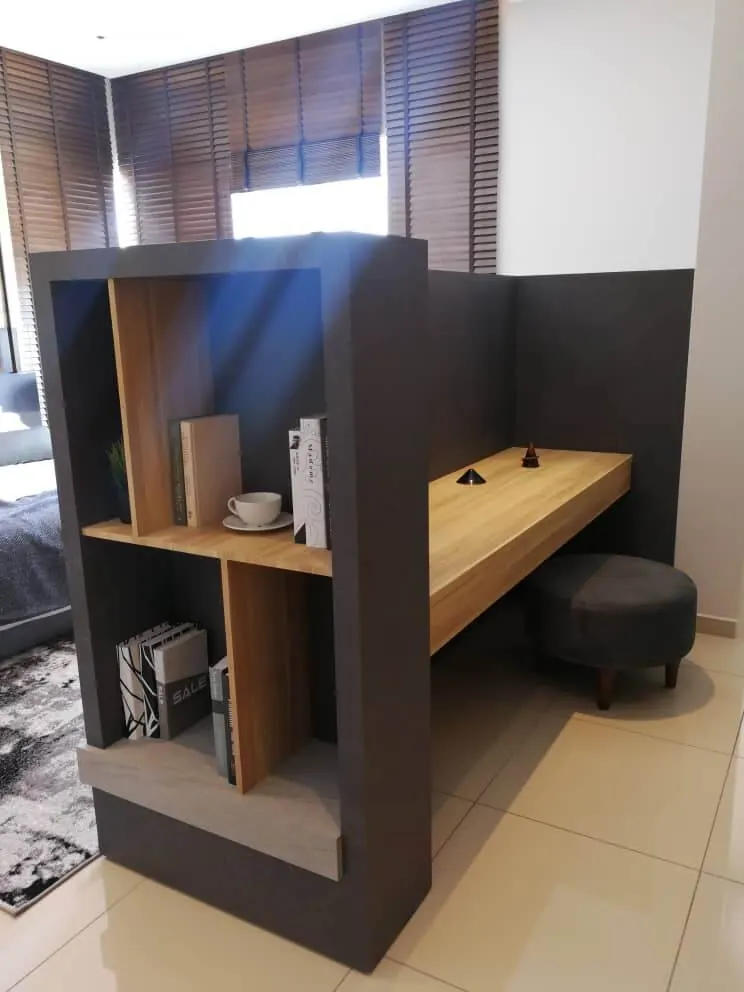 Built-in study desk in wood finish joined to a grey bookshelf divider, with a stool underneath