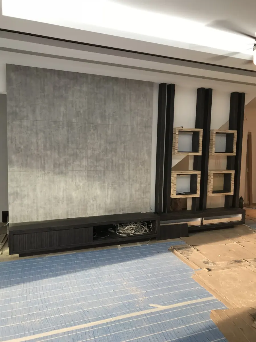 Grey concrete-look panel TV wall with dark wood posts and box shelves, during installation